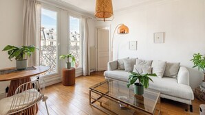 A modern living room with a sofa, coffee table, and chairs. There are potted plants and a hanging light fixture.