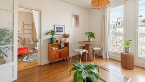A modern living room with a round wooden table, white chairs, and a hanging light fixture.