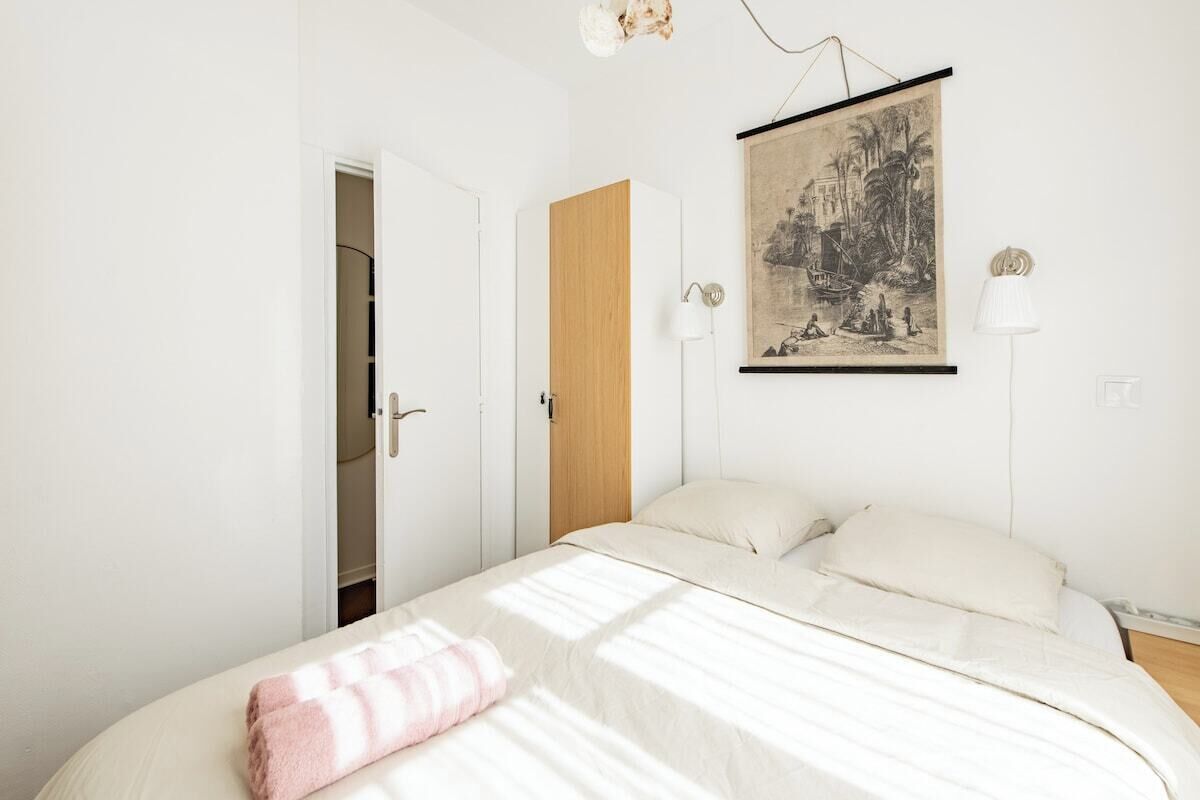 Een slaapkamer met een bed, een houten garderobe, een deur en een aan de muur hangend schilderij.