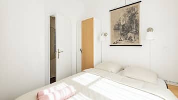 Een slaapkamer met een bed, een houten garderobe, een deur en een aan de muur hangend schilderij.
