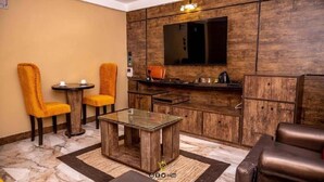 Un salon moderne avec un mur d’accent en bois, un téléviseur à écran plat, une table basse en verre et deux fauteuils jaunes.