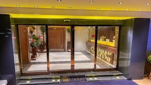 L’entrée d’un hôtel, avec une porte en verre, un comptoir d’accueil et un tapis bleu orné du nom de l’hôtel.