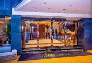 A hotel entrance with a glass door, a reception desk, and a "Joker" logo on the floor mat. - Joker Hotel and Suites  (Benin City)