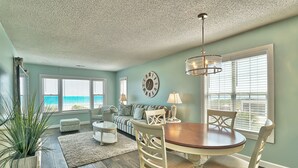 A living room with a dining table, chairs, a sofa, and a large window with a view of the ocean. - Dog Friendly-Sandy Dunes-Sleeps 8-3br/2b-Oceanfront-WIFI (North Myrtle Beach)