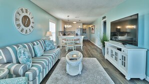 A living room with a sofa, coffee table, TV stand, and a dining area with a table and chairs. - Dog Friendly-Sandy Dunes-Sleeps 8-3br/2b-Oceanfront-WIFI (North Myrtle Beach)