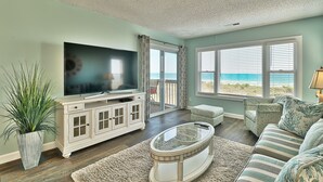 A living room with a TV, a glass coffee table, a sofa, a potted plant, and a view of the ocean through large windows. - Dog Friendly-Sandy Dunes-Sleeps 8-3br/2b-Oceanfront-WIFI (North Myrtle Beach)