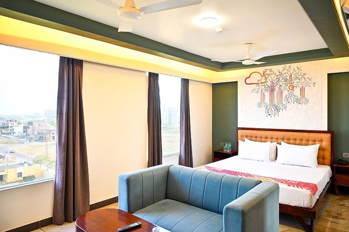 Une chambre d’hôtel comprenant un lit, un canapé, un ventilateur de plafond, une grande fenêtre et une œuvre d’art murale.