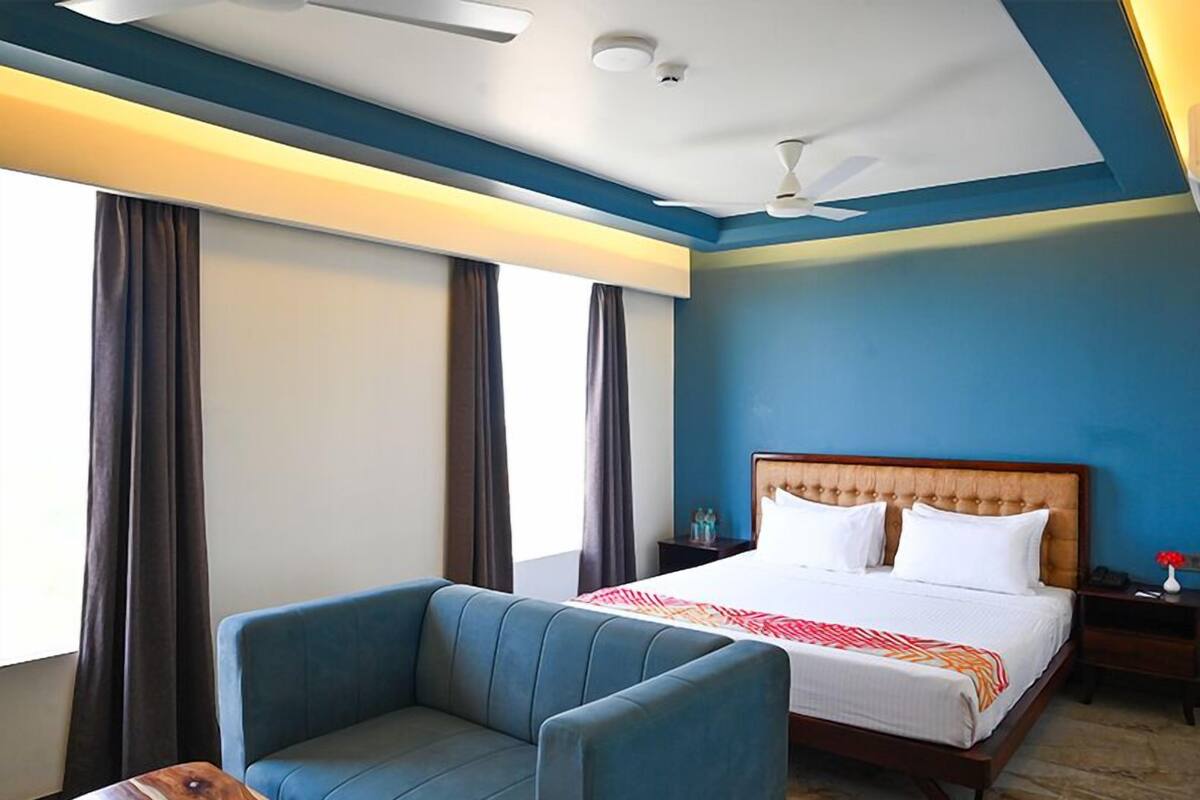 Une chambre d’hôtel avec un lit, un canapé bleu, un ventilateur de plafond et une table de chevet avec une lampe.