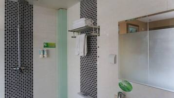 Un baño con ducha, lavamanos, espejo y perchero para toallas.