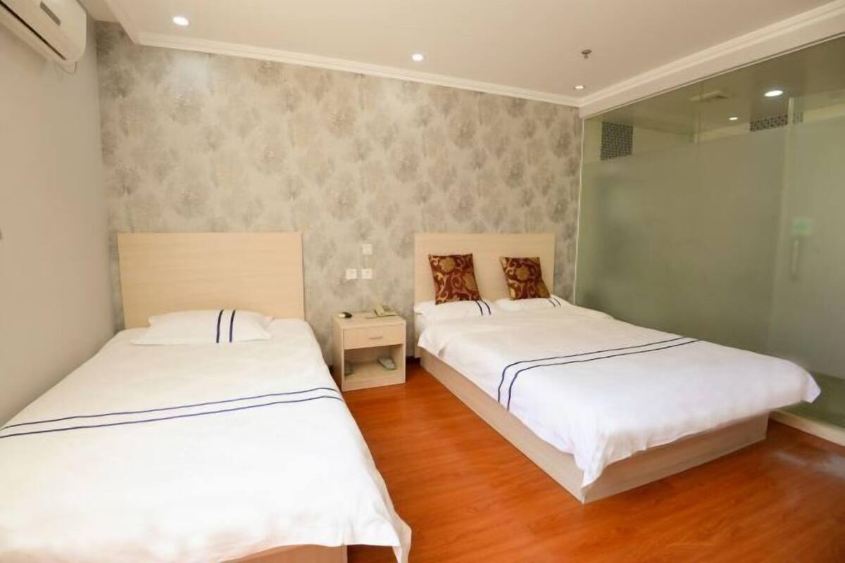 Een hotelkamer met twee bedden, een nachtkastje en een douchecabine van glas.