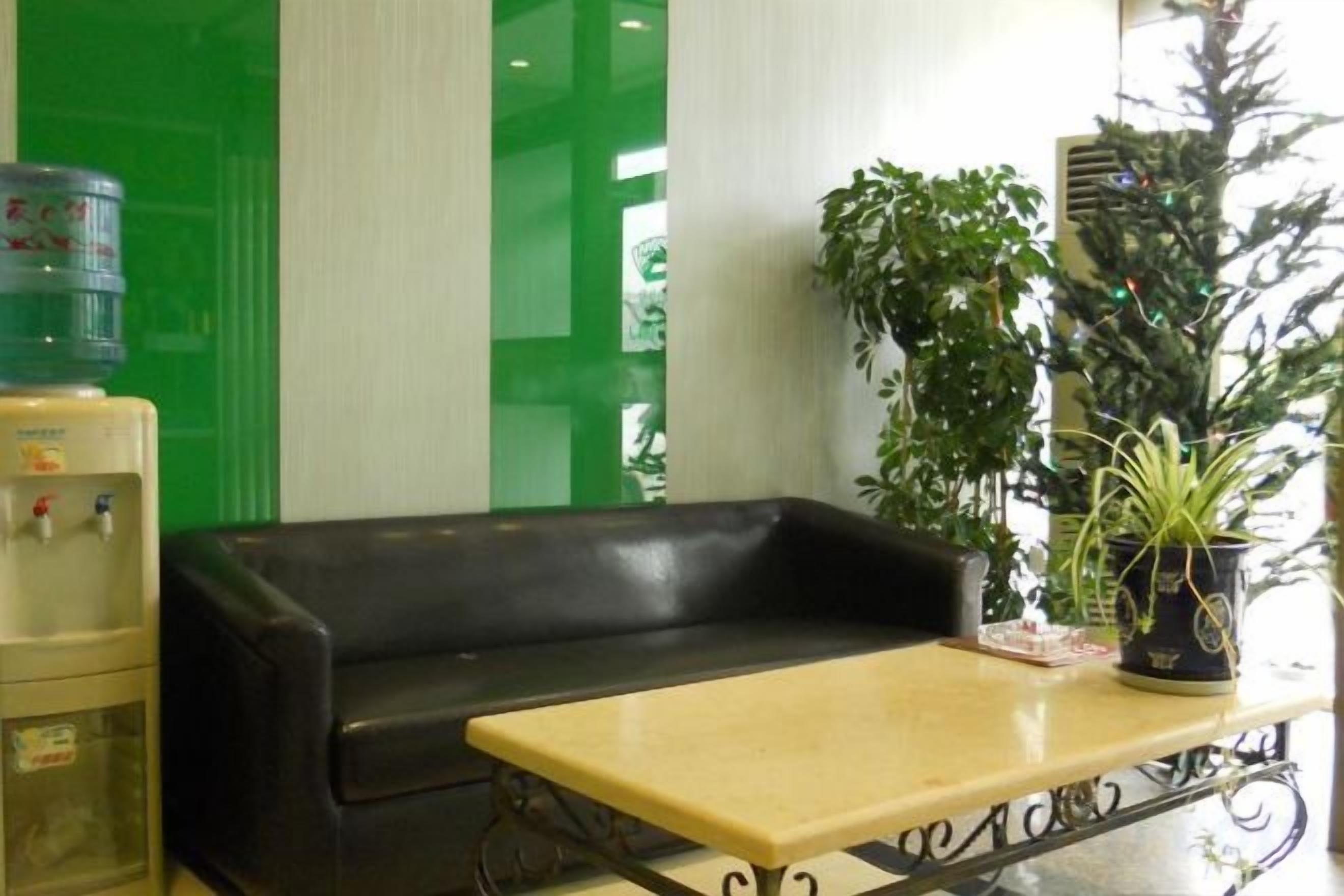 A reception area with a black sofa, a small table, a water dispenser, and potted plants.