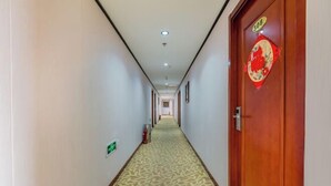 Un couloir d’hôtel avec un tapis à motifs, une porte en bois ornée d’un décor rouge et un extincteur fixé au mur.