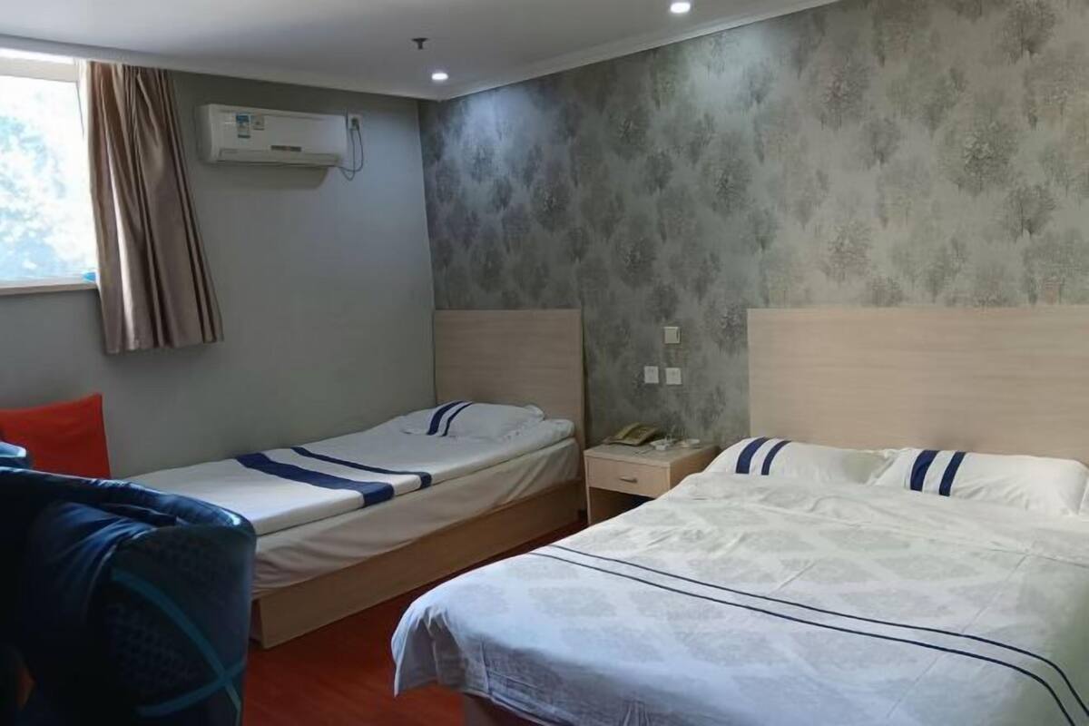 Een hotelkamer met twee bedden, een bureau, een stoel, een airconditioning en een raam met gordijnen.