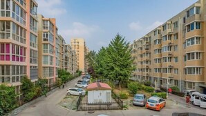 Un immeuble résidentiel à plusieurs étages, doté de balcons et d’une cour intérieure agrémentée d’arbres et où sont garées des voitures.