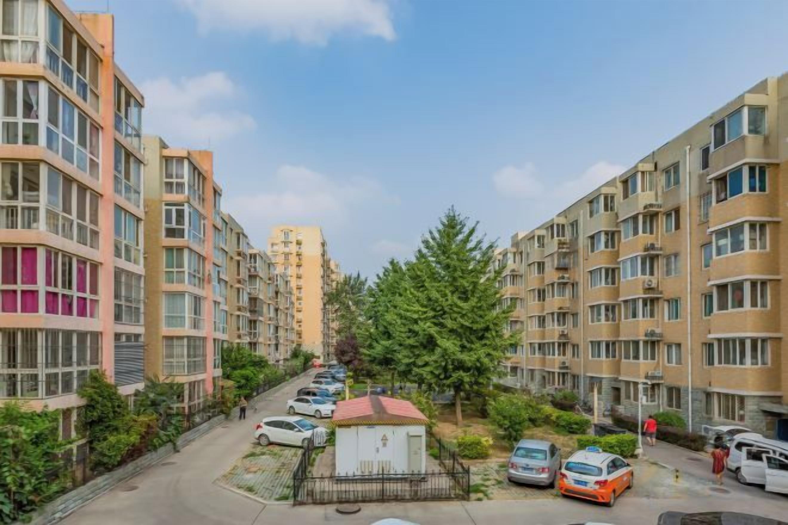 A residential area with multi-story apartment buildings, a parking lot, and a small fenced garden area.