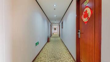 A hotel hallway with a carpeted floor, a wooden door with a red decoration, and a fire extinguisher on the wall.