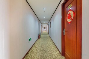 Ein Hotelgang mit Teppichboden, einer Holztür mit roter Dekoration und einem Feuerlöscher an der Wand.