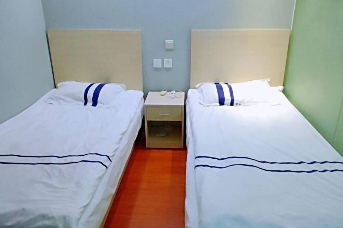 Een tweepersoonskamer met twee eenpersoonsbedden, een klein nachtkastje en een bedtafel.