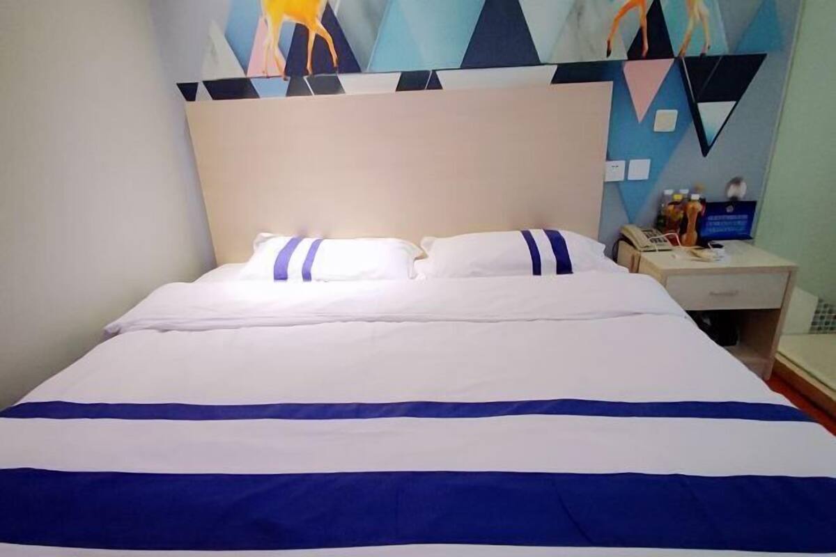 Een hotelkamer met een bed, kussens, een nachtkastje en een muur met geometrische patronen.
