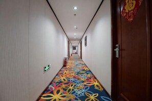 Un couloir d’hôtel avec un tapis à motifs, des portes des deux côtés et un panneau sur le mur de droite.