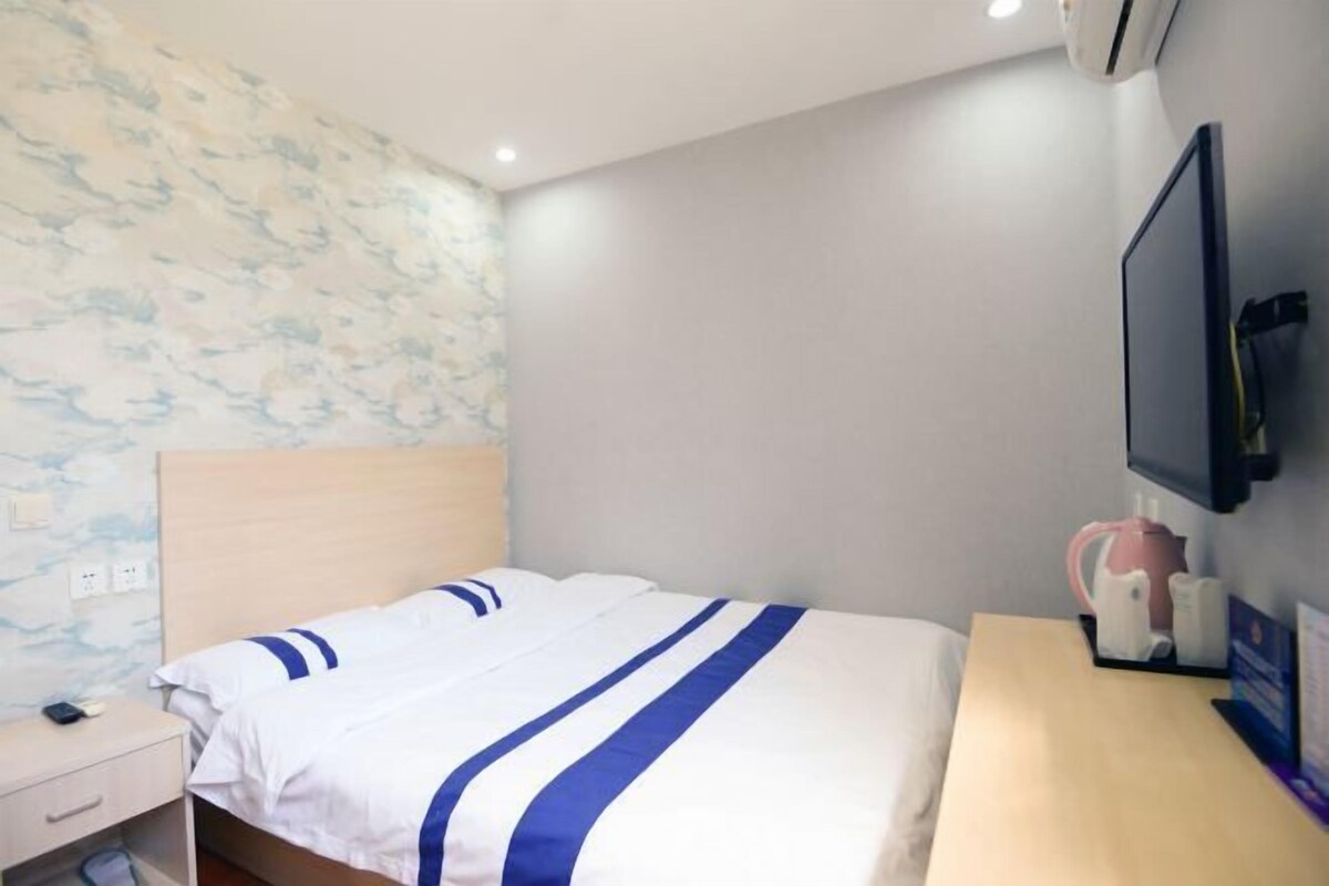 A hotel room with a bed, a nightstand, a desk, a television, and a wall-mounted air conditioner.