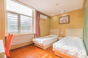 Ein Zimmer mit zwei Betten, einem Fenster mit Jalousien, einer Klimaanlage, einem gerahmten Bild an der Wand und einem Stuhl.