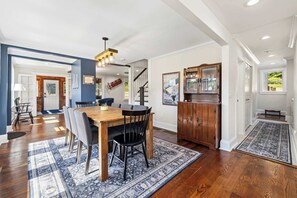 Uma sala de jantar com mesa e cadeiras de madeira, um tapete estampado e um lustre.