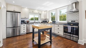 A modern kitchen with white cabinets, stainless steel appliances, and a wooden table.