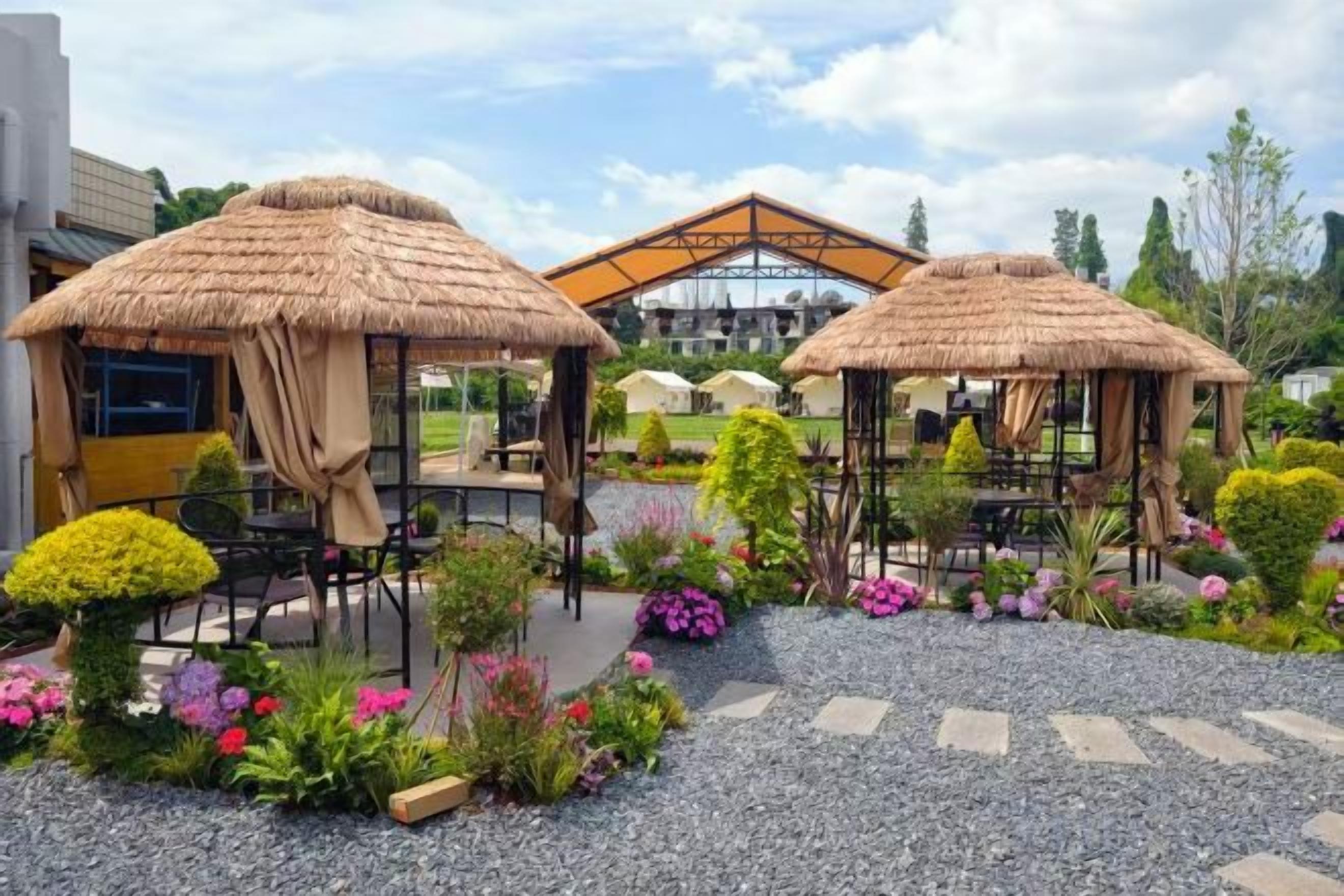 Een tuin met gebouwen met rieten daken, zitplaatsen en aangelegde bloembedden.