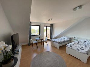 Une chambre moderne et bien éclairée, équipée d’un lit, d’un bureau et d’une chaise. Une fenêtre laisse entrer la lumière naturelle et offre une vue sur l’extérieur.