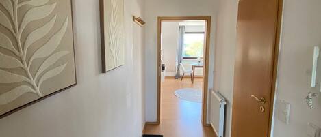 A hallway with a wooden floor, a door on the right, and a ceiling light fixture.
