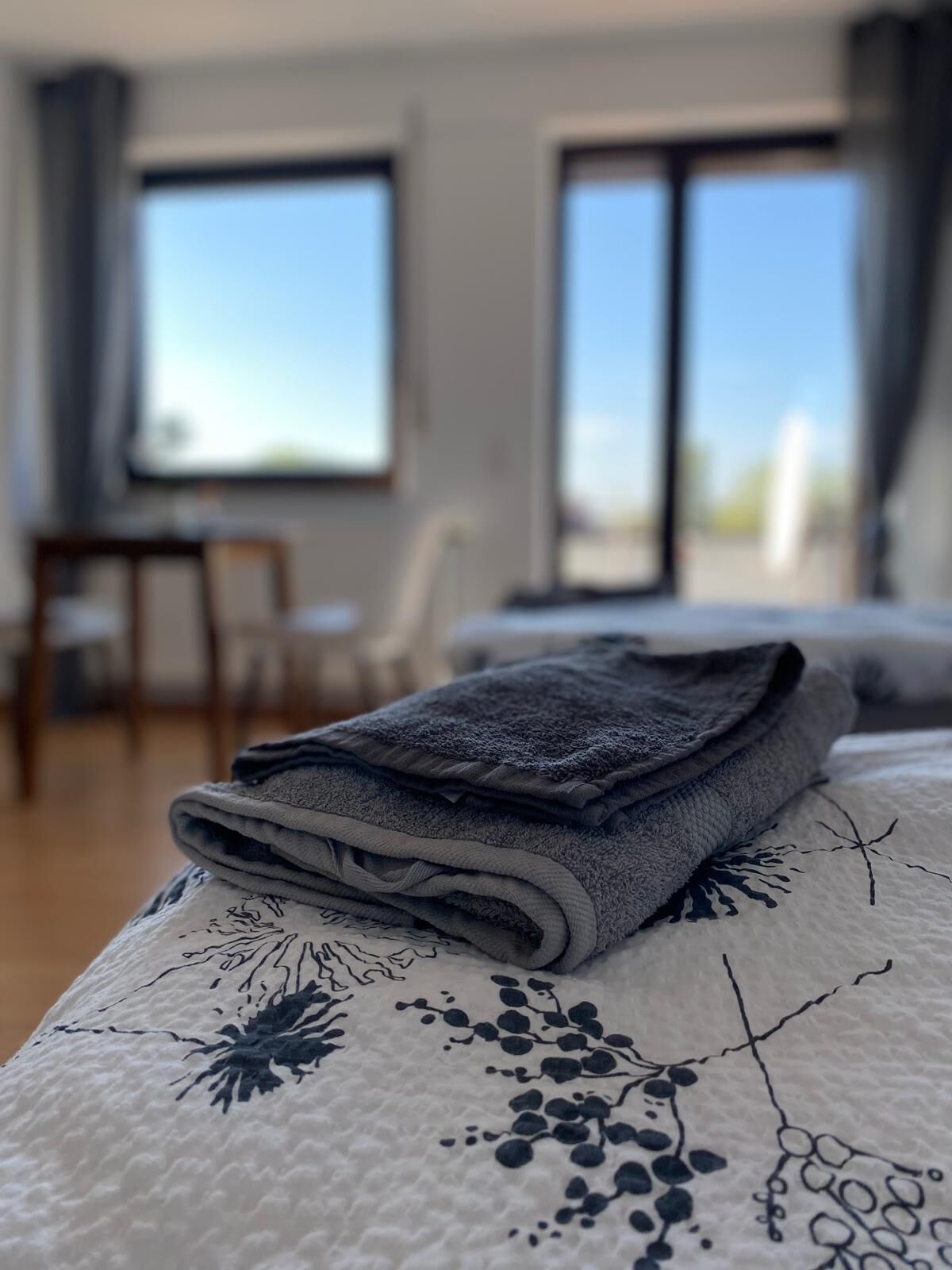 A neatly made bed with a floral-patterned bedspread and a folded gray towel on top.