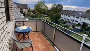 A balcony with a table and chairs, a view of neighboring houses, and a cloudy sky. - Am Quellberg Apartments Recklinghausen (Recklinghausen)