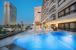 Una piscina con sillas de descanso y sombrillas, rodeada de edificios modernos.