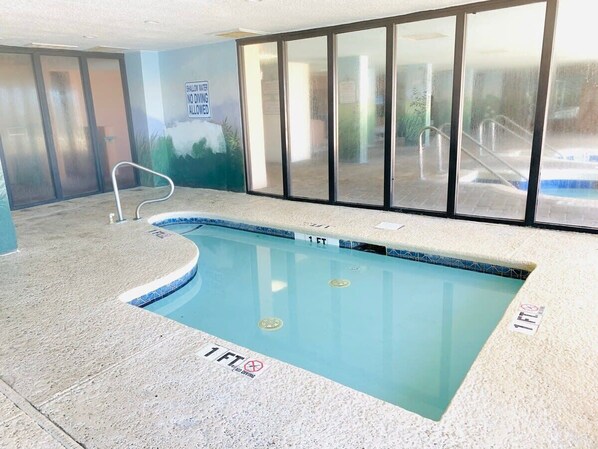 An indoor swimming pool with a 1 FT depth marking, a no diving sign, and a view of a building with a glass door. - Sand Castle Resort #14, Gorgeous Oceanview (Myrtle Beach)