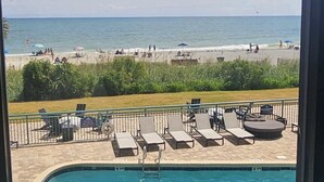 En swimmingpool med krystalklart, blåt vand, udsigt til stranden samt liggestole og parasoller på terrassen.