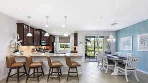 Una cocina moderna con armarios de madera oscura, una isla central con taburetes altos e iluminación colgante.
