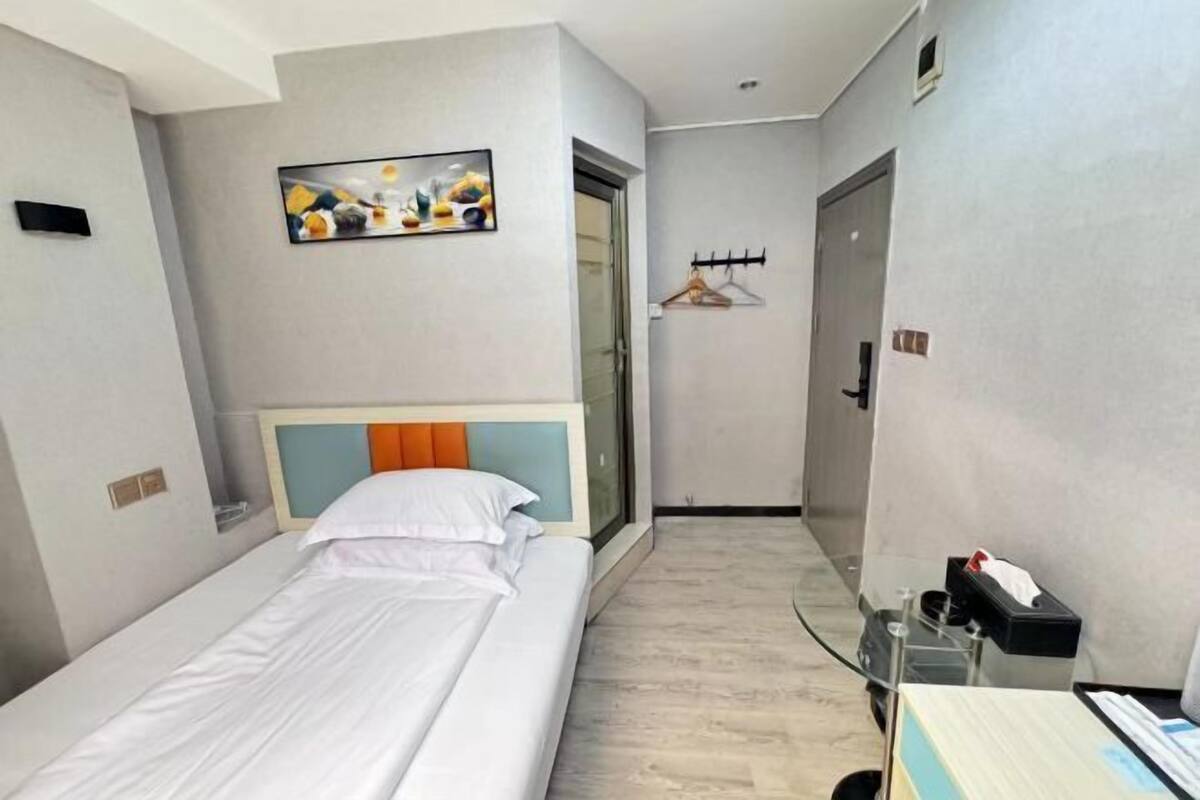 A hotel room with a bed, a TV mounted on the wall, a coat rack, and a door leading to another room.