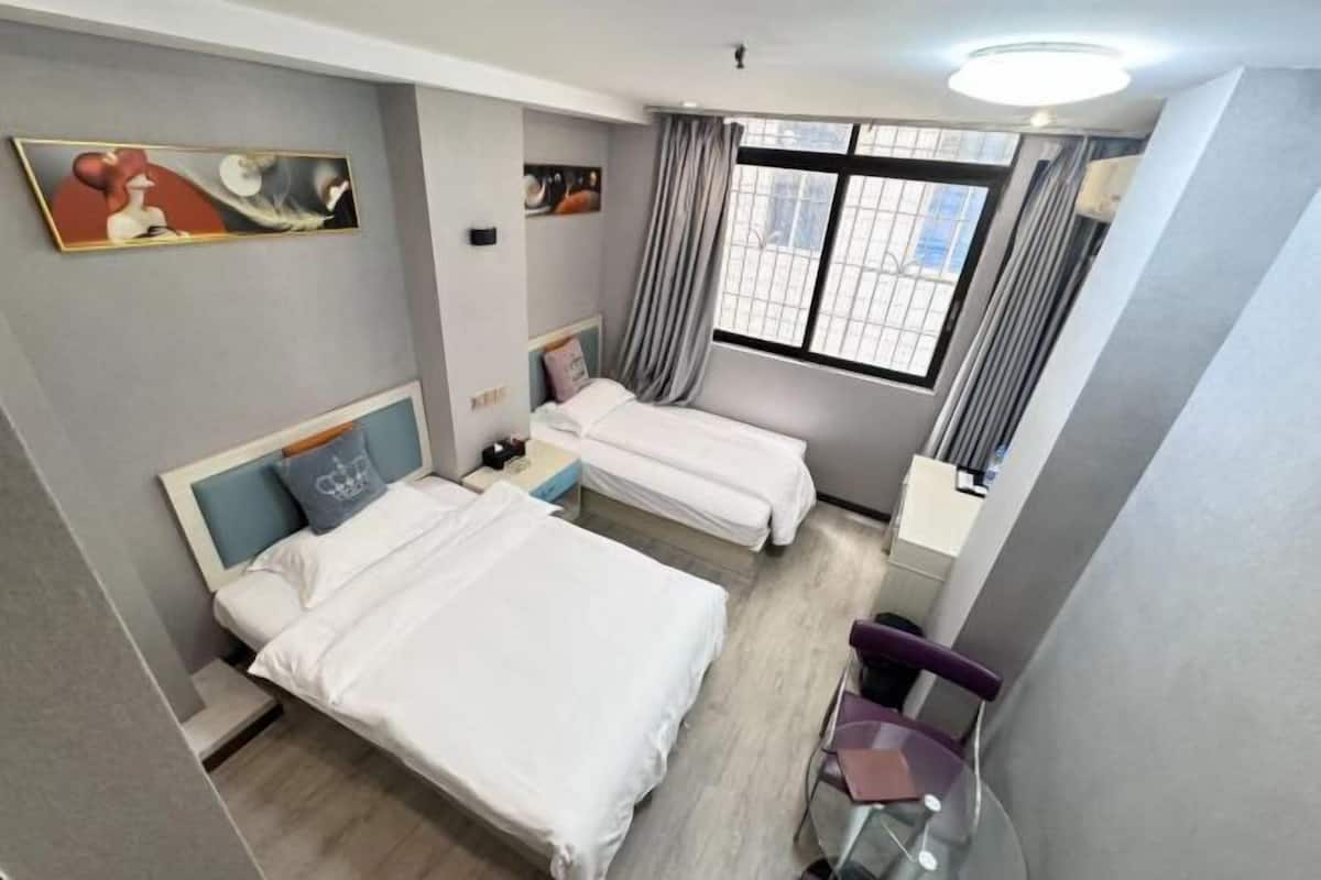 A hotel room with two beds, a desk, a chair, and artwork on the walls.