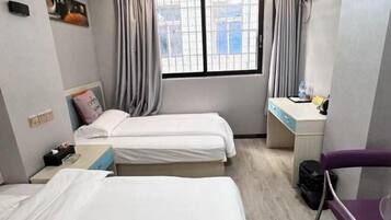 A hotel room with two beds, a desk, a chair, and a window with curtains.