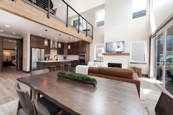 Relax in a spacious living area with a mezzanine level, featuring a fireplace, flat-screen TV, and modern kitchen with dark cabinetry and stainless steel appliances.