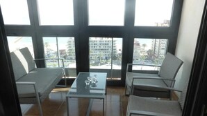 Un balcon avec deux chaises, une petite table et une vue sur des immeubles et des palmiers.
