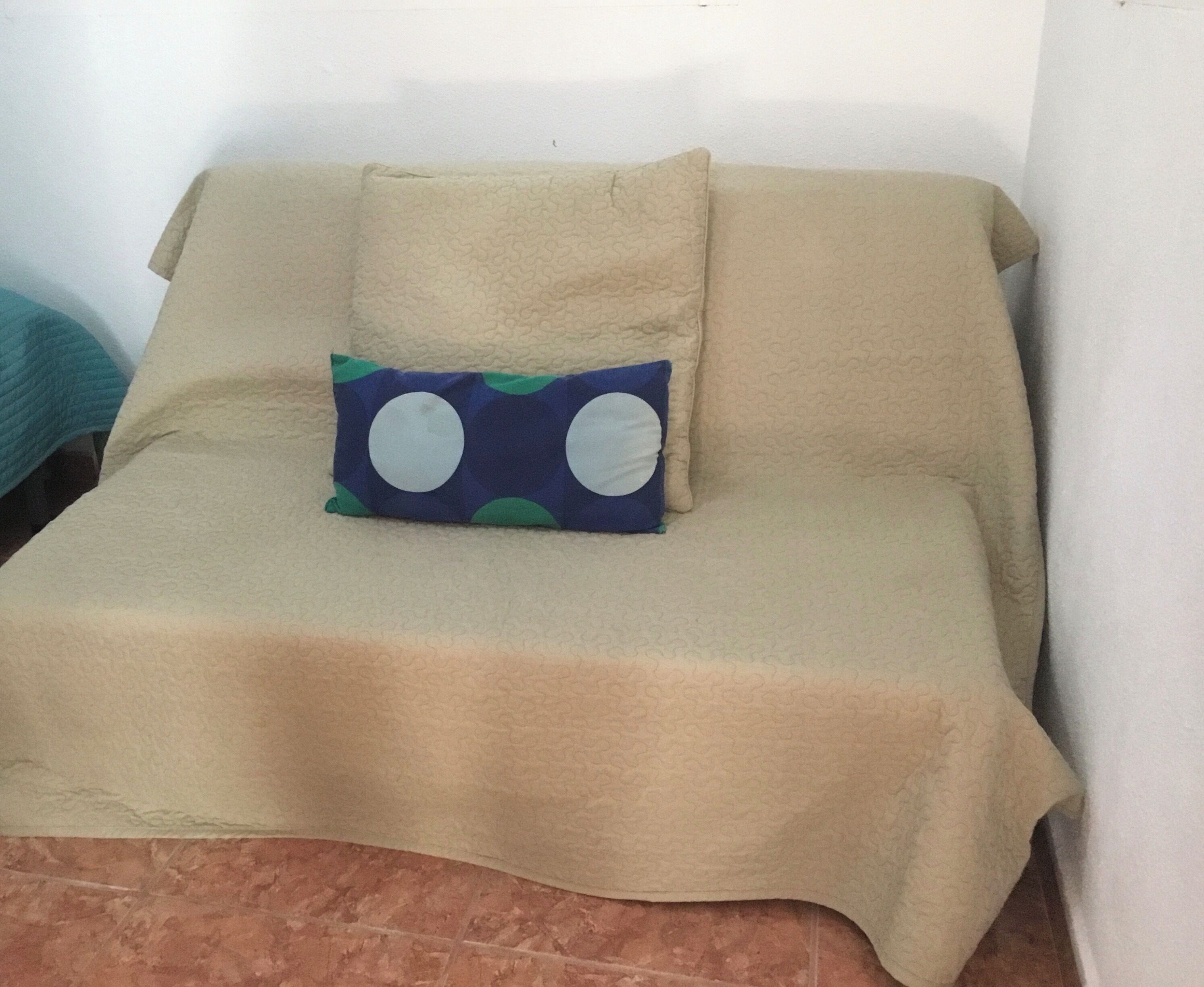 A bed with a beige cover and a pillow with a blue and green pattern.