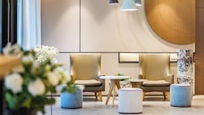 Un hall d’hôtel moderne au design minimaliste, avec des fauteuils en cuir, des tables rondes et des luminaires suspendus.