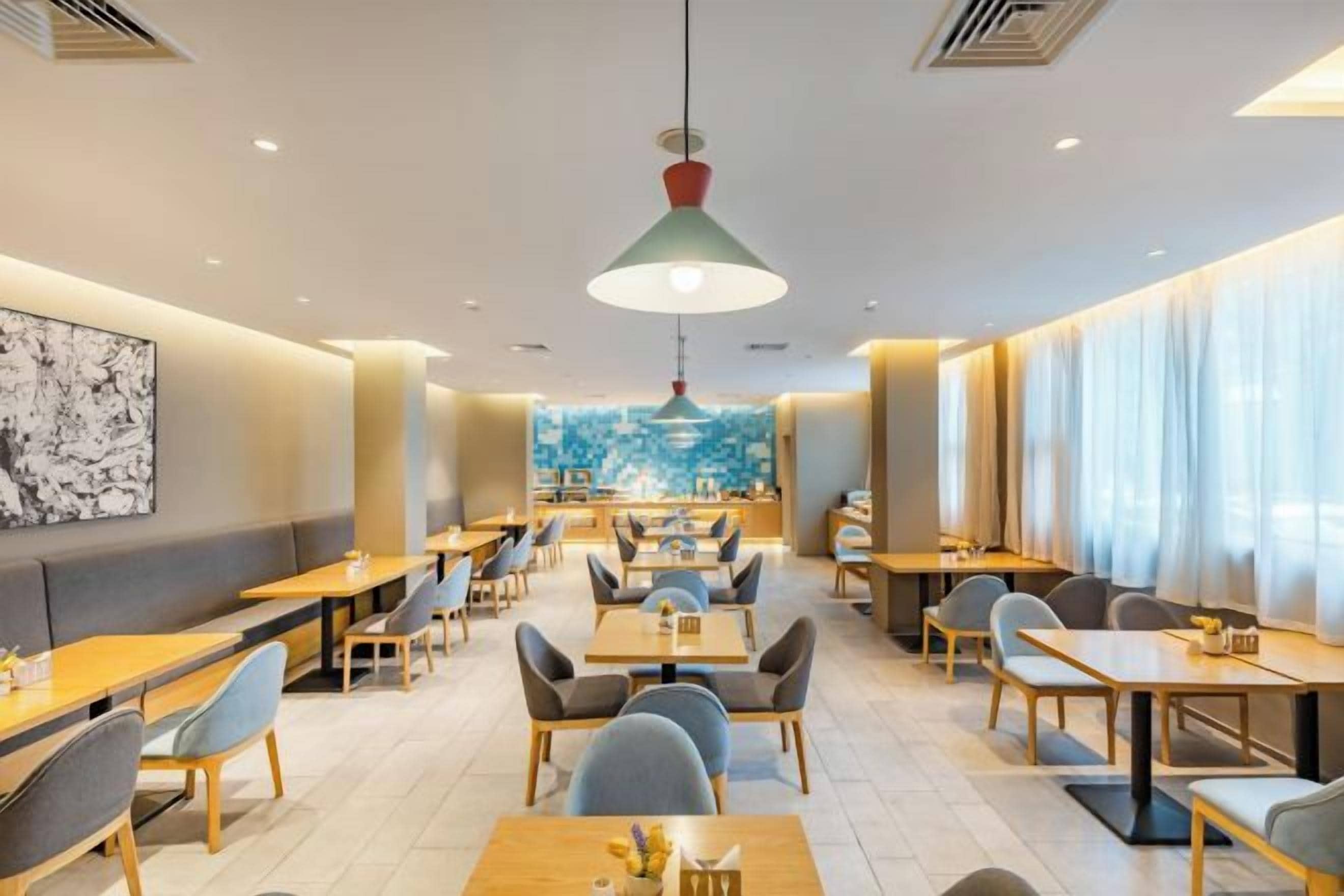 Um restaurante moderno com cabines e mesas, uma luminária pendente grande e vista para a cidade.