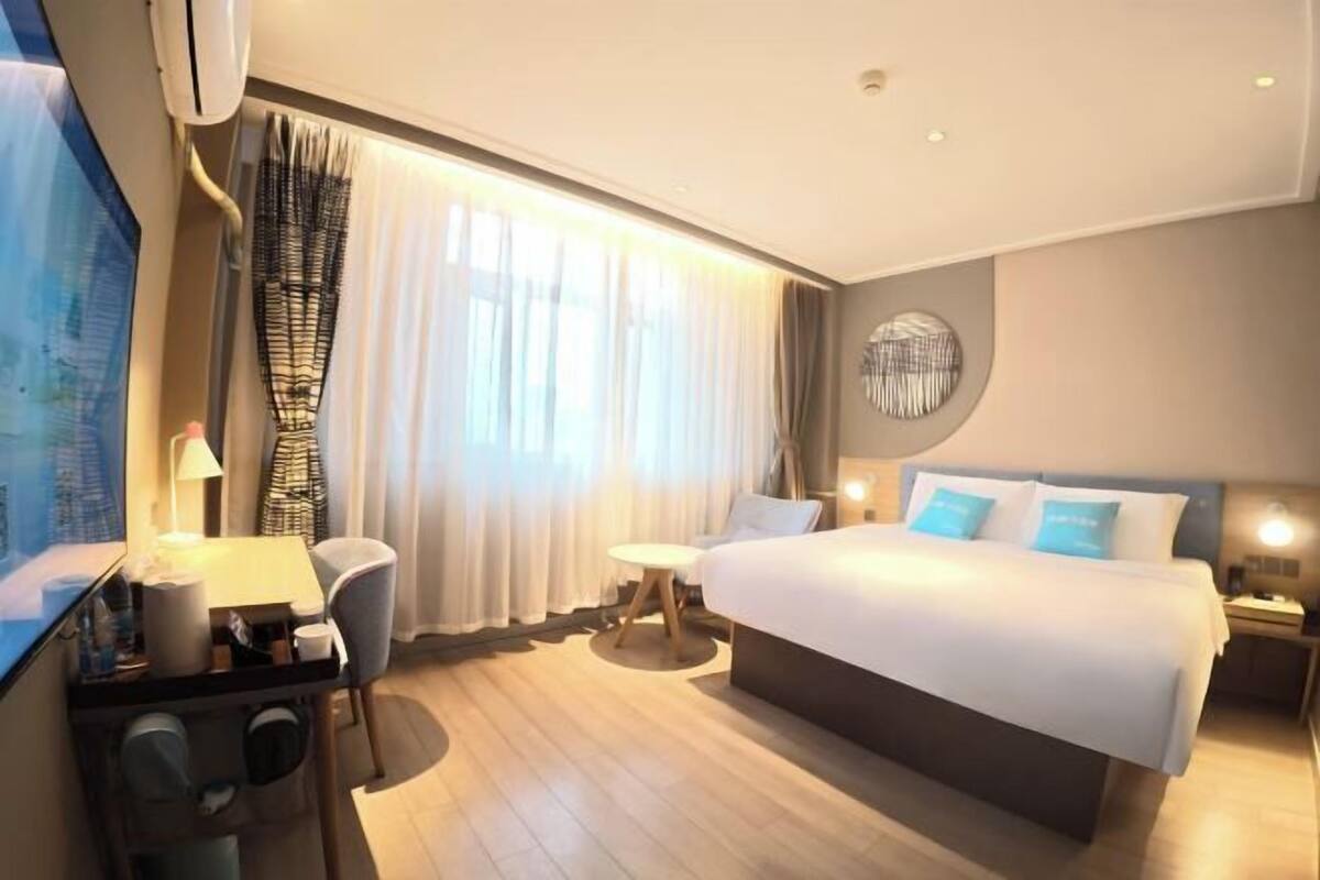 A hotel room with a bed, bedside table, lamp, and a TV.