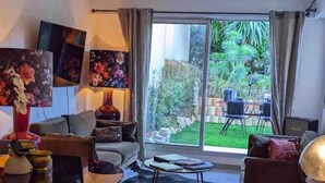Een moderne woonkamer met een grote glazen deur die uitkomt op een tuin. Er is een bank, een salontafel en een vloerkleed met een koeienhuidpatroon.