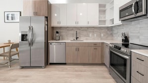 Une cuisine moderne dotée d’appareils électroménagers en acier inoxydable, de meubles de cuisine en bois clair et d’un dosseret carrelé.