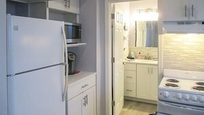 Uma cozinha compacta com armários brancos, micro-ondas embutido, fogão e um pequeno balcão.