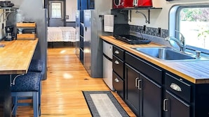 Una cocina compacta con una mesa y un banco de madera, un lavamanos y un microondas rojo.